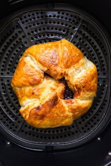A croissant is sitting in an air fryer.