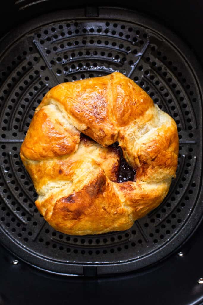A croissant is sitting in an air fryer.