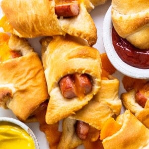 A plate with hot dogs wrapped in crescent rolls and dipping sauce.