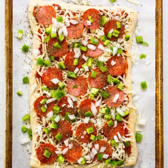Pepperoni pizza on a baking sheet with green onions.