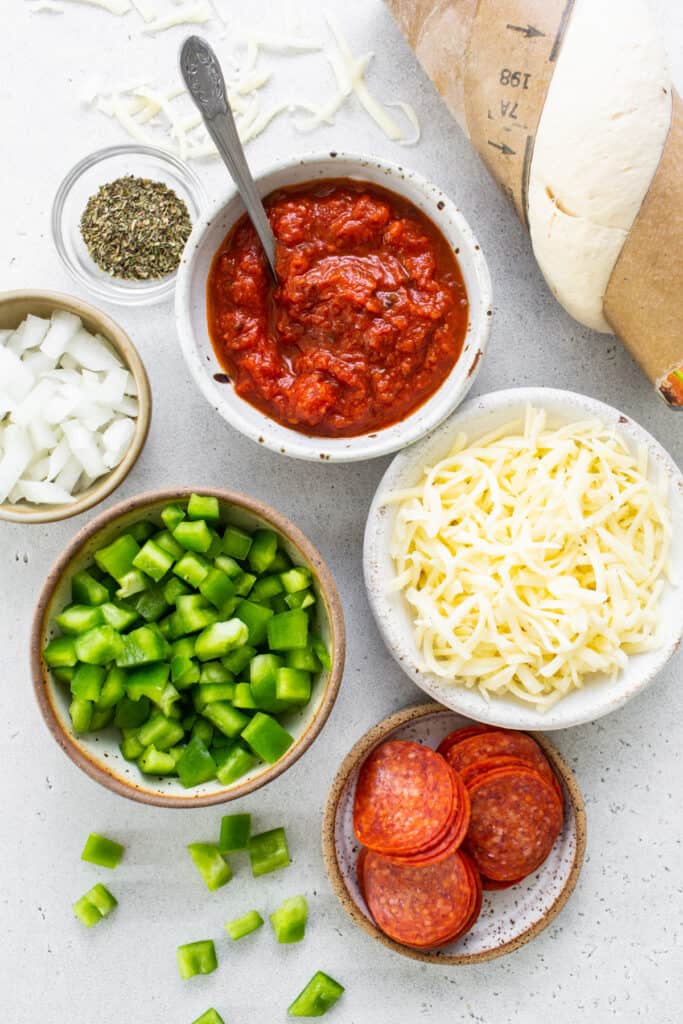 Ingredients for a pizza with pepperoni, peppers, onions and cheese.