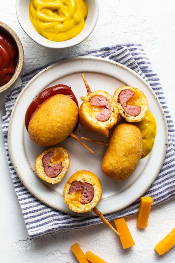 Hot dog on a stick with ketchup and cheese on a plate.