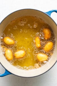 A blue pot filled with oil and fried doughnuts.