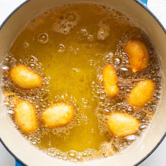 A blue pot filled with oil and fried doughnuts.