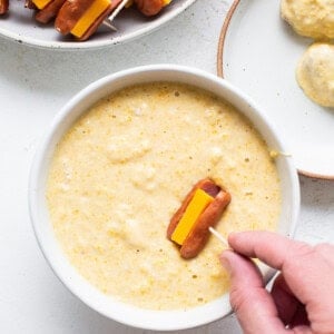 A person is dipping a hot dog into a bowl of dip.