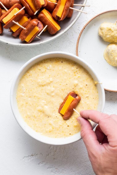 A person is dipping a hot dog into a bowl of dip.