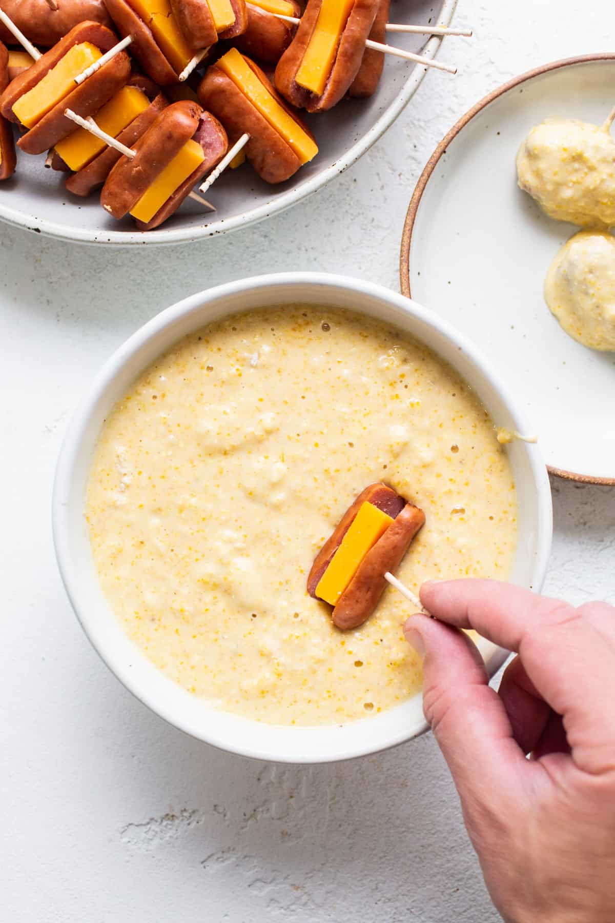 A person is dipping a hot dog into a bowl of dip.