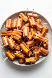 Cheesy hot dogs on toothpicks on a plate.