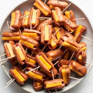 Cheesy hot dogs on toothpicks on a plate.