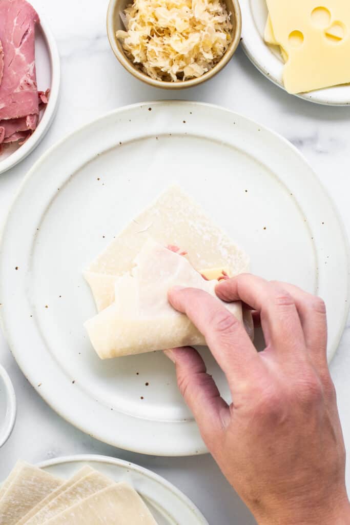 A person cutting a piece of cheese on a plate.
