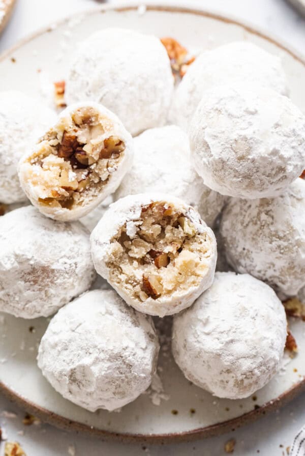 A plate full of powdered sugar cookies with pecans.