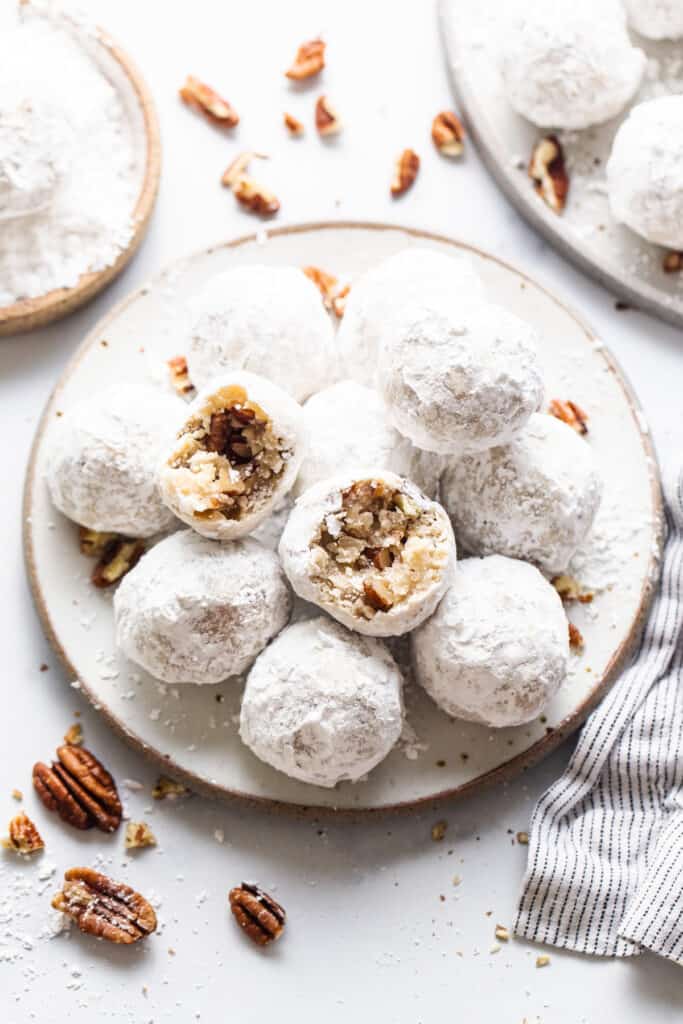 Powdered sugar cookies with pecans on a plate.