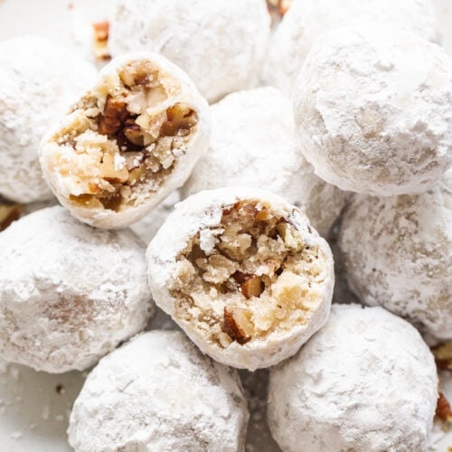 Powdered sugar balls with pecans on a white plate.