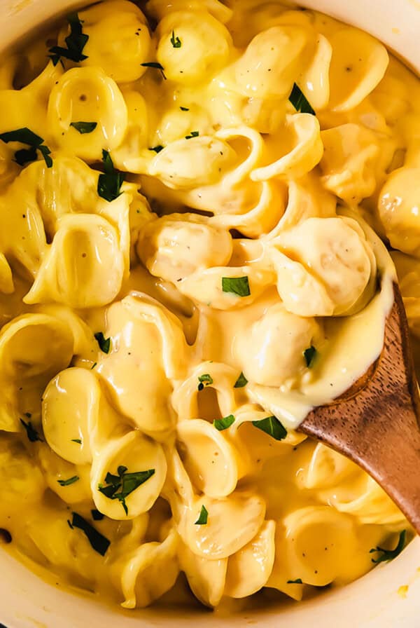 Cheesy pasta in a white bowl with a wooden spoon.