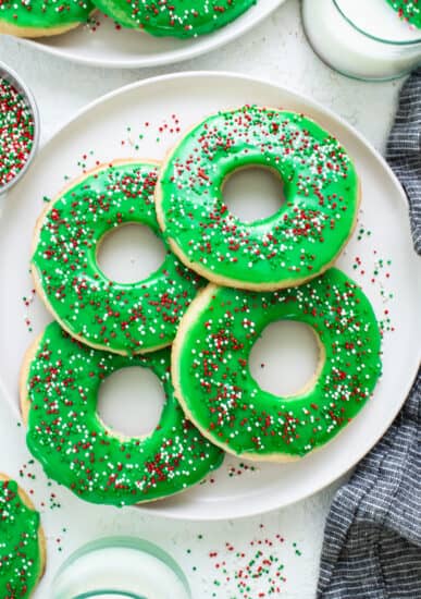 Donuts with green icing and sprinkles on a plate.
