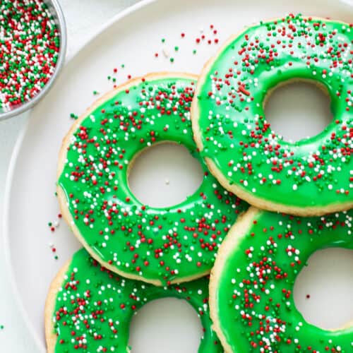 Donuts with green icing and sprinkles on a plate.
