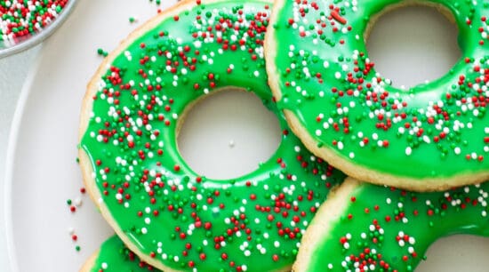 Donuts with green icing and sprinkles on a plate.