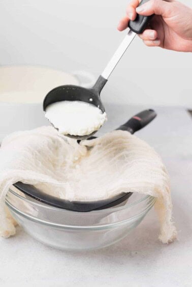 A person pouring ricotta into a glass bowl.