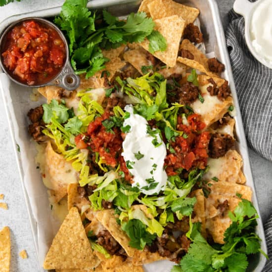 Mexican nachos on a tray with sour cream and guacamole.