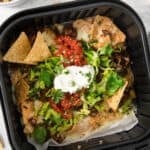 Nachos in a black container with sour cream and guacamole.