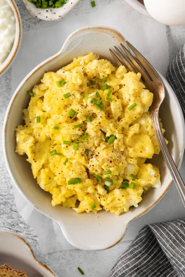 A bowl of scrambled eggs with chives and bread.