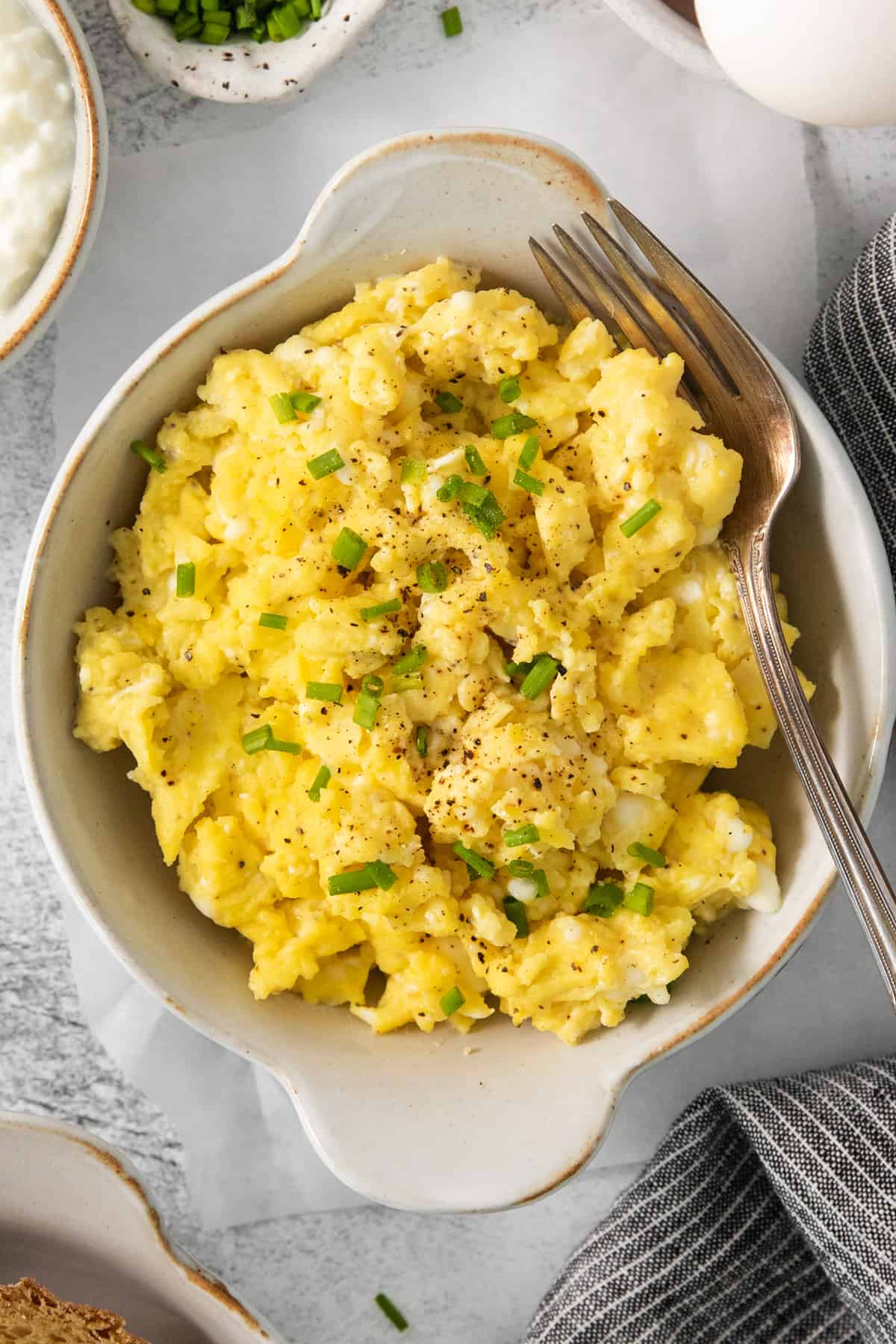 A bowl of scrambled eggs with chives and bread.