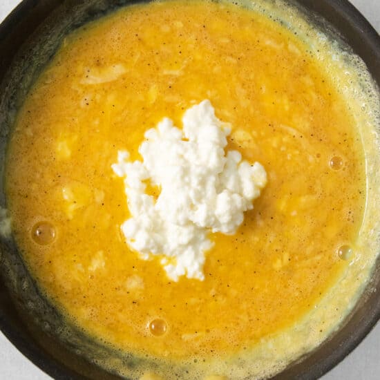 A frying pan with a yellow sauce and feta cheese.