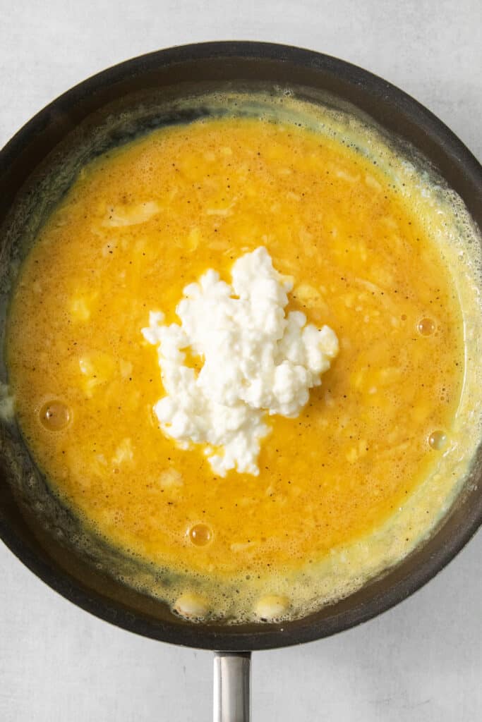 A frying pan with a yellow sauce and feta cheese.