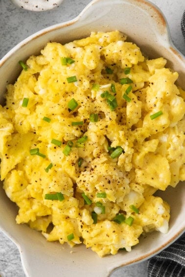 Scrambled eggs in a bowl with chives and sour cream.