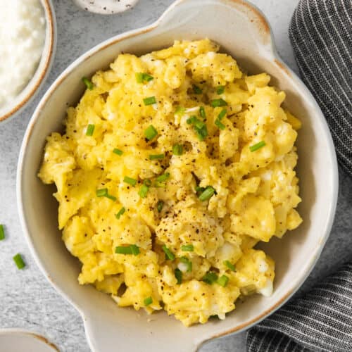 Scrambled eggs in a bowl with chives and sour cream.