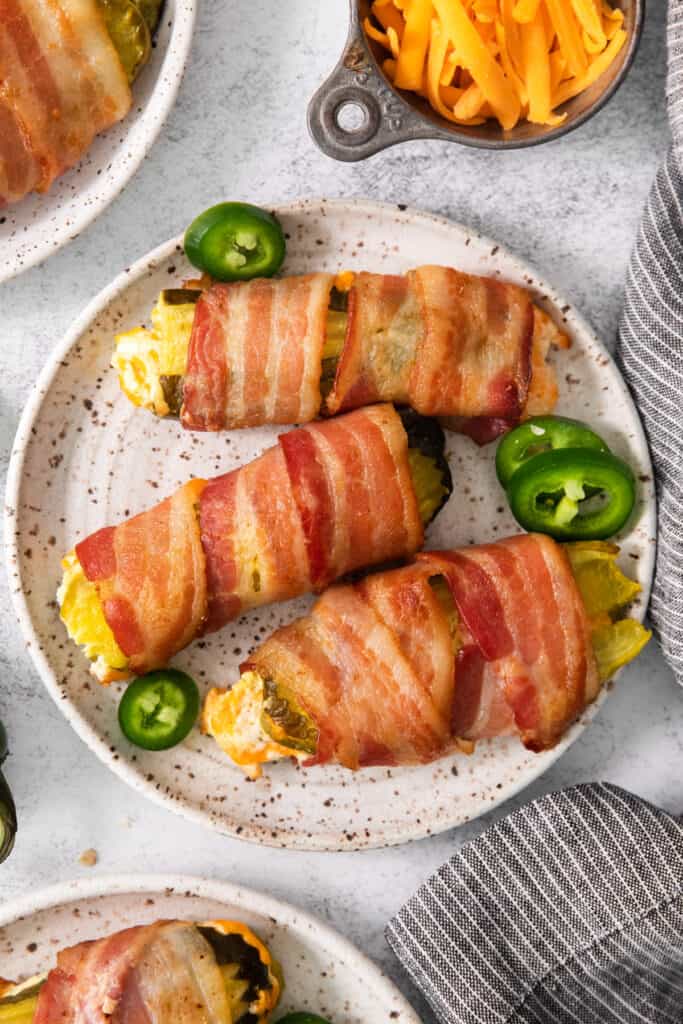 Bacon wrapped peppers on a plate with cheese and jalapenos.