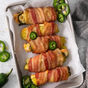 Bacon wrapped peppers on a baking sheet.