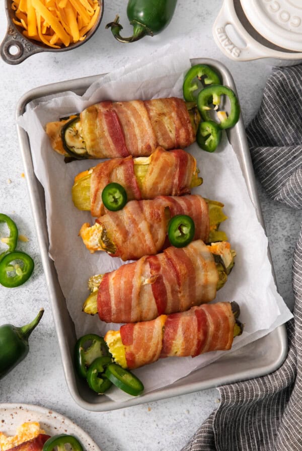 Bacon wrapped peppers on a baking sheet.