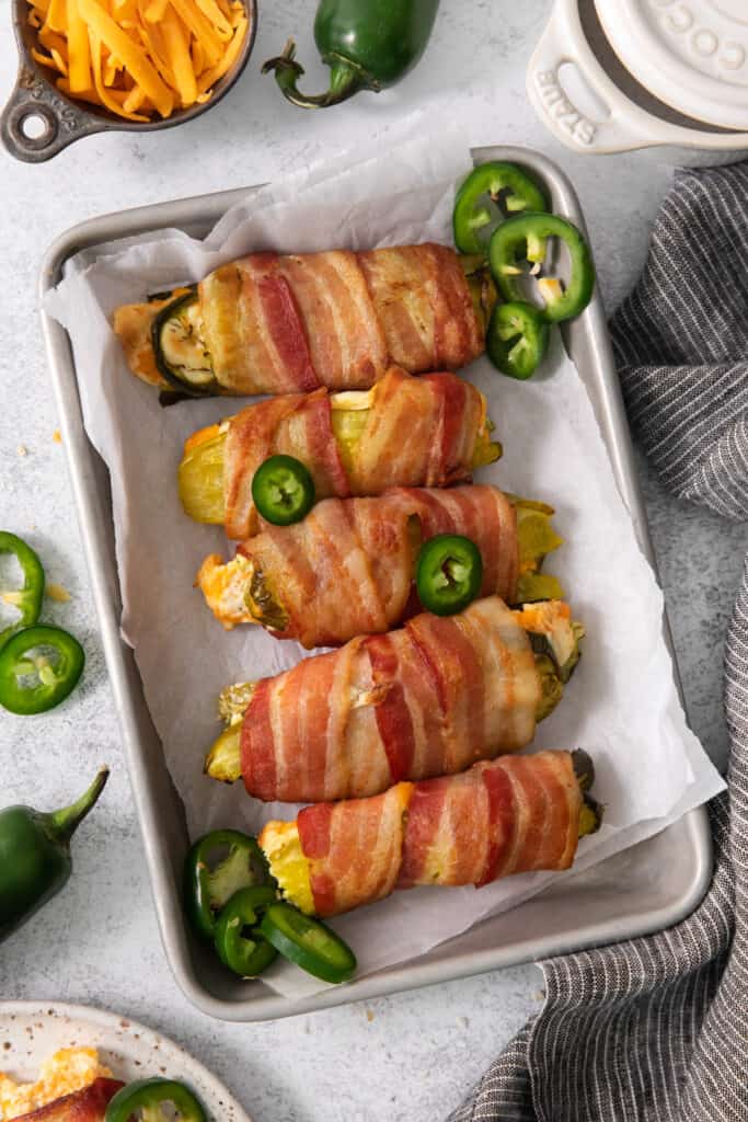 Bacon wrapped peppers on a baking sheet.
