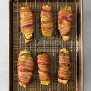 Bacon wrapped peppers on a baking sheet.