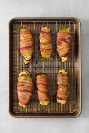 Bacon wrapped peppers on a baking sheet.