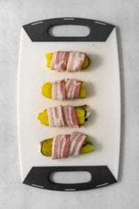 Bacon wrapped zucchini on a cutting board.