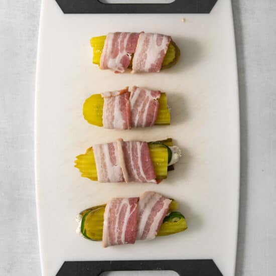 Bacon wrapped zucchini on a cutting board.