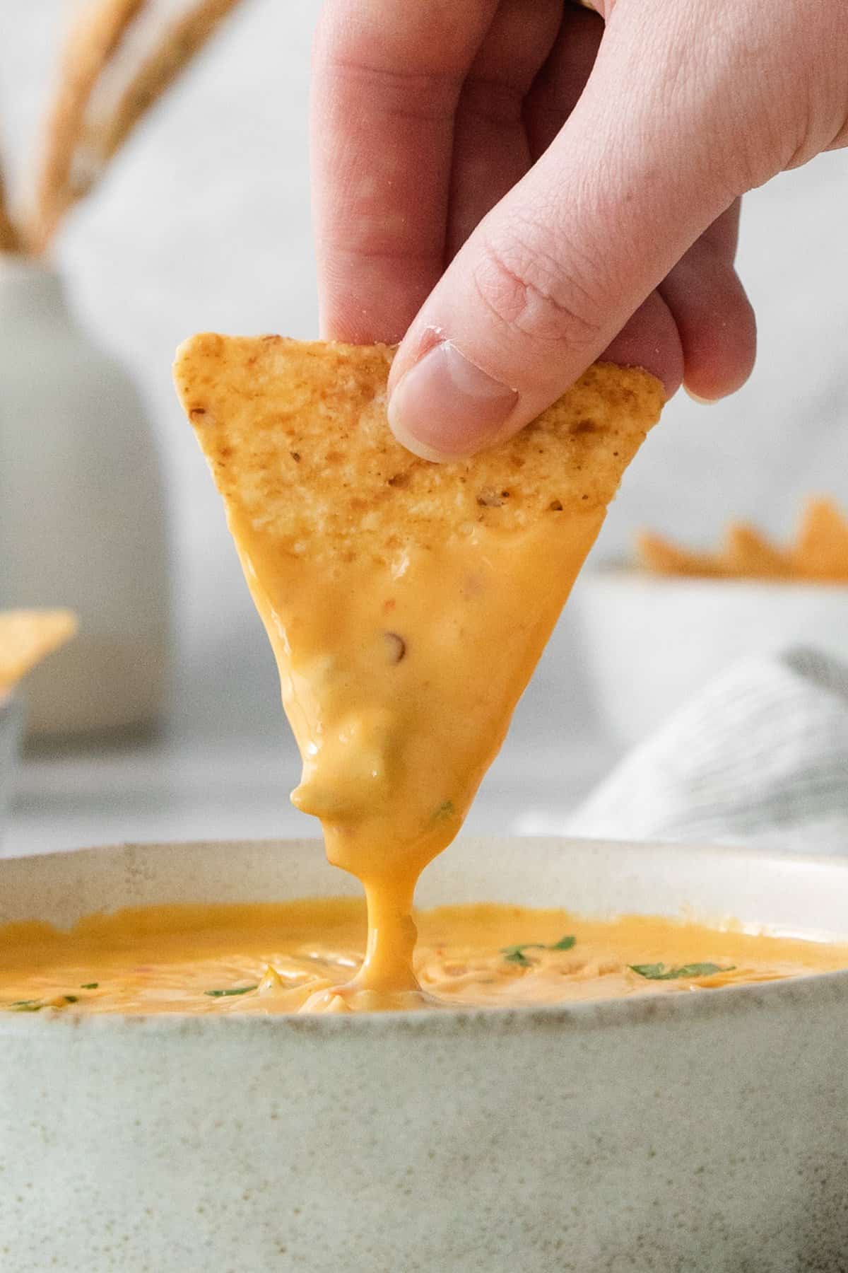 A person dipping a tortilla chip into a bowl of cheese dip.