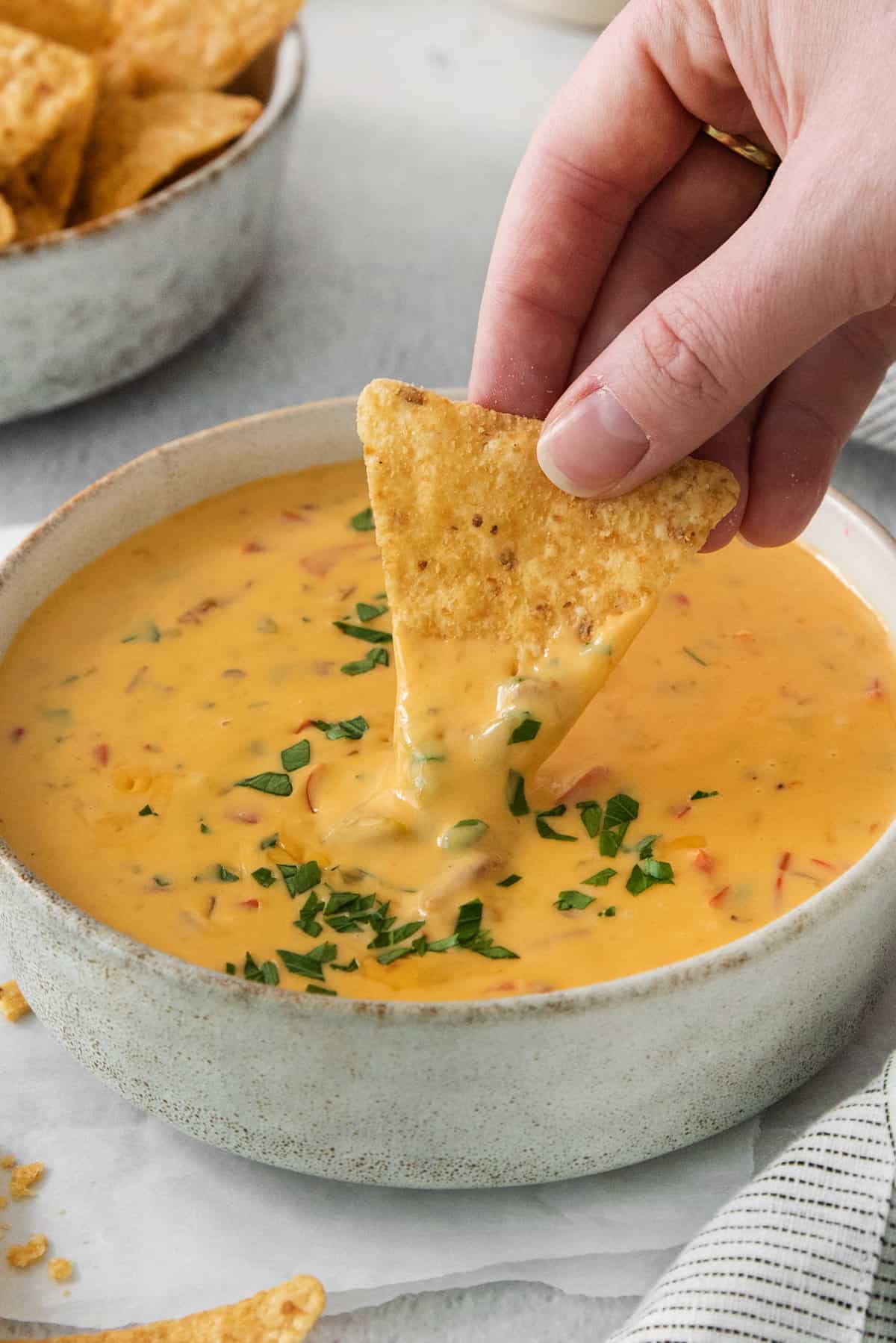 A person dipping a tortilla chip into a bowl of cheese dip.