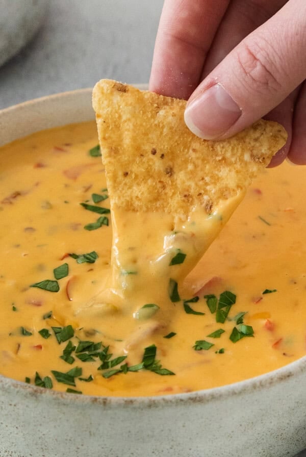 A person dipping a tortilla chip into a bowl of cheese dip.