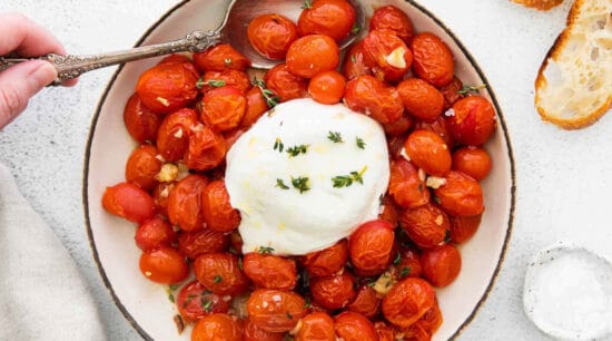 A bowl of roasted tomatoes with ricotta and a spoon.