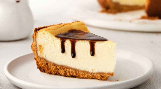 A slice of cheesecake with chocolate drizzle on a plate.