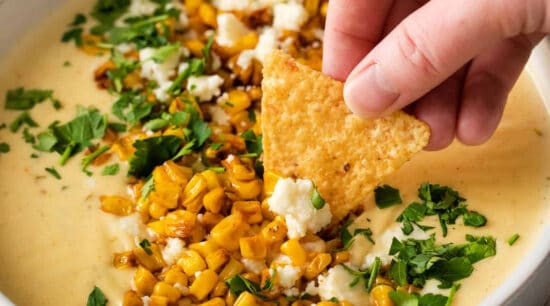 A person dipping a tortilla chip into a bowl of corn dip.