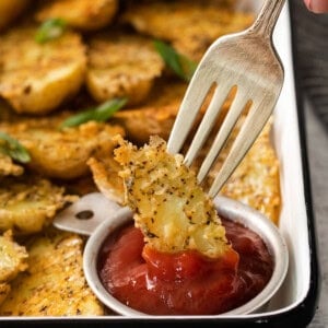 A person is holding a fork over a tray of potato wedges with ketchup.