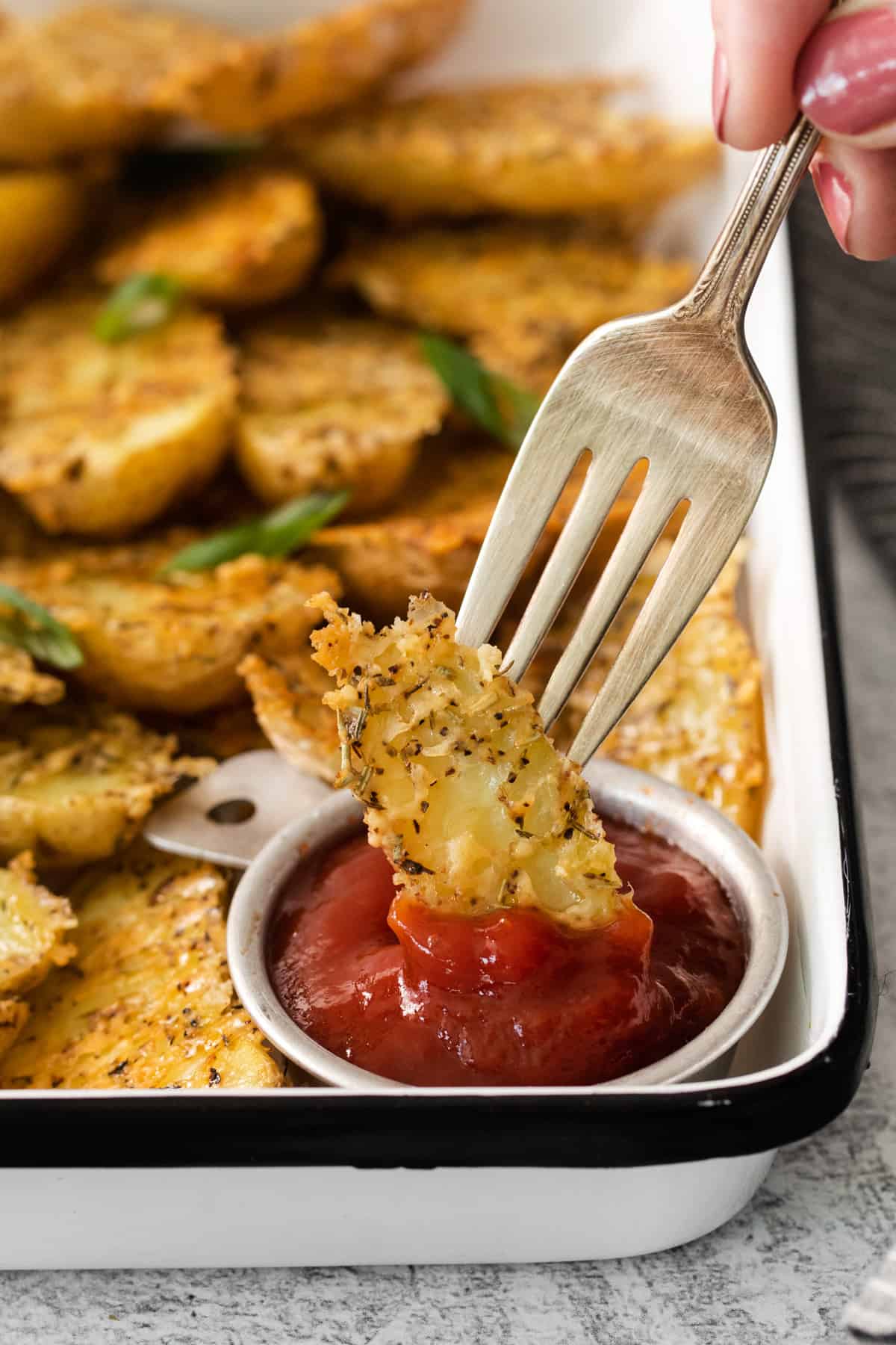 A person is holding a fork over a tray of potato wedges with ketchup.