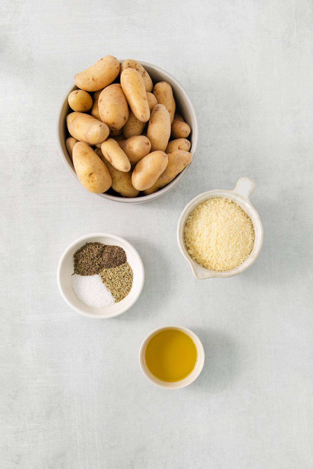 A bowl of potatoes, parmesan cheese, olive oil and spices on a white background.