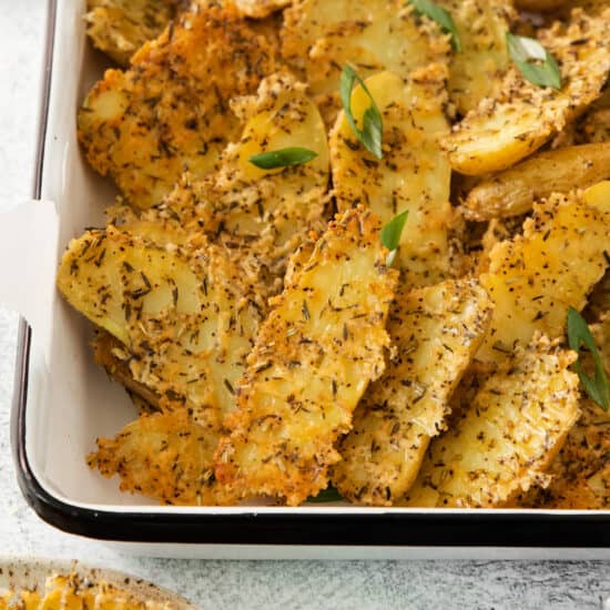 Roasted potato wedges in a baking dish with herbs.