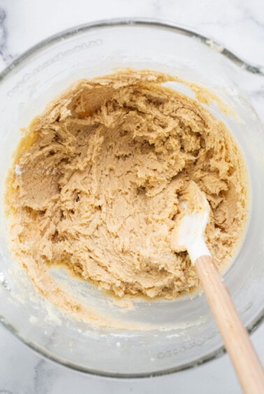 Peanut butter cookie dough in a bowl with a wooden spoon.
