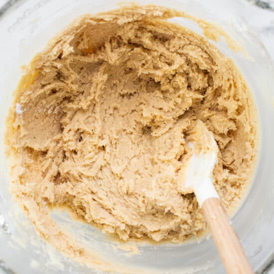 Peanut butter cookie dough in a bowl with a wooden spoon.